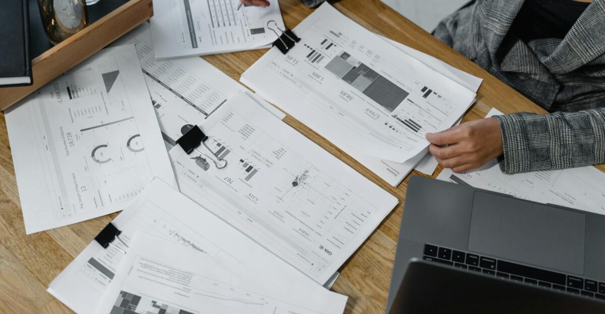 Woman analyzing financial data and reports on a wooden desk with a laptop showcasing analytics in a workspace
