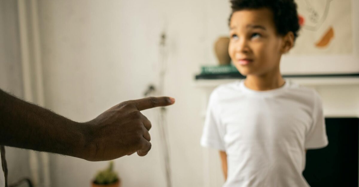 A father points and scolds his son indoors emphasizing discipline