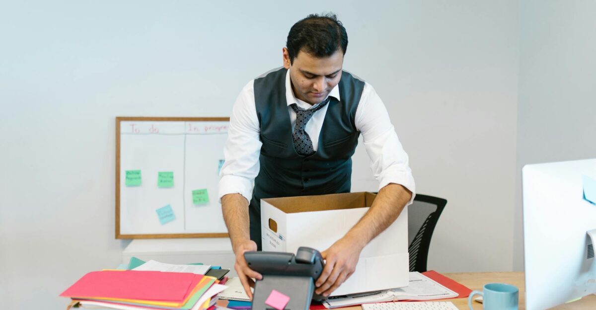 A man packing up his desk in an office setting with papers and a phone
