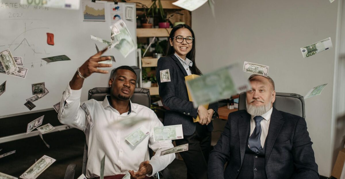 Diverse business team celebrating success with cash raining indoors in office