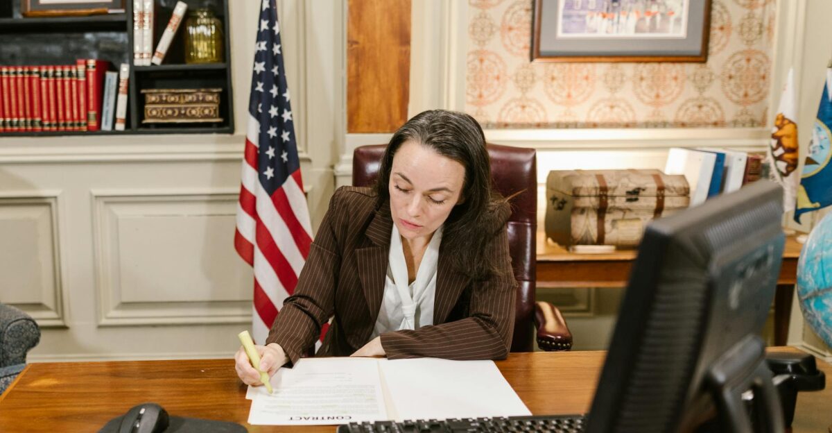 Female attorney in a law office signing legal documents at her desk surrounded by legal books and symbols of justice