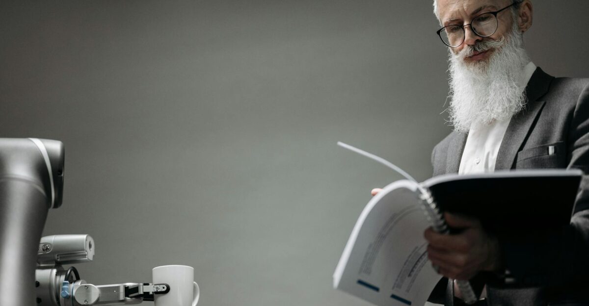 Elderly man reads as a robotic arm holds a coffee cup showcasing technology integration