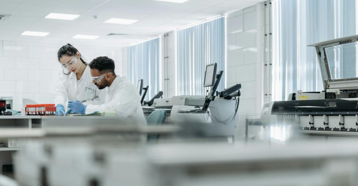 Two scientists working in a high-tech laboratory setting wearing protective eyewear and gloves