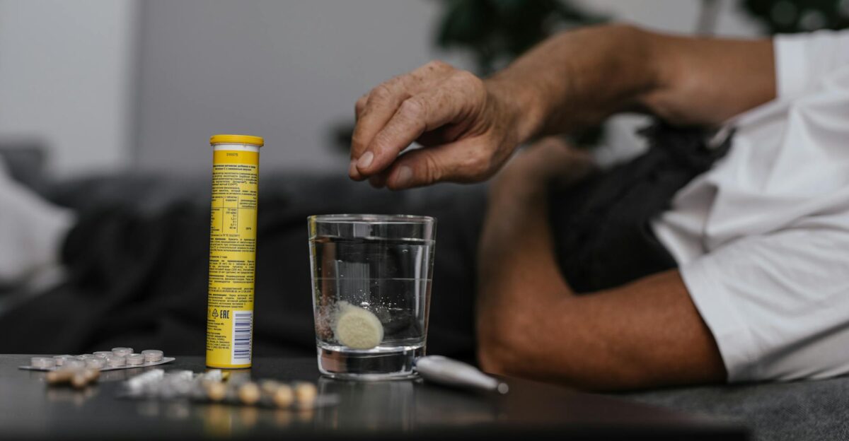 Elderly man lays in bed while dissolving a soluble medicine in water indicating health and wellness home care