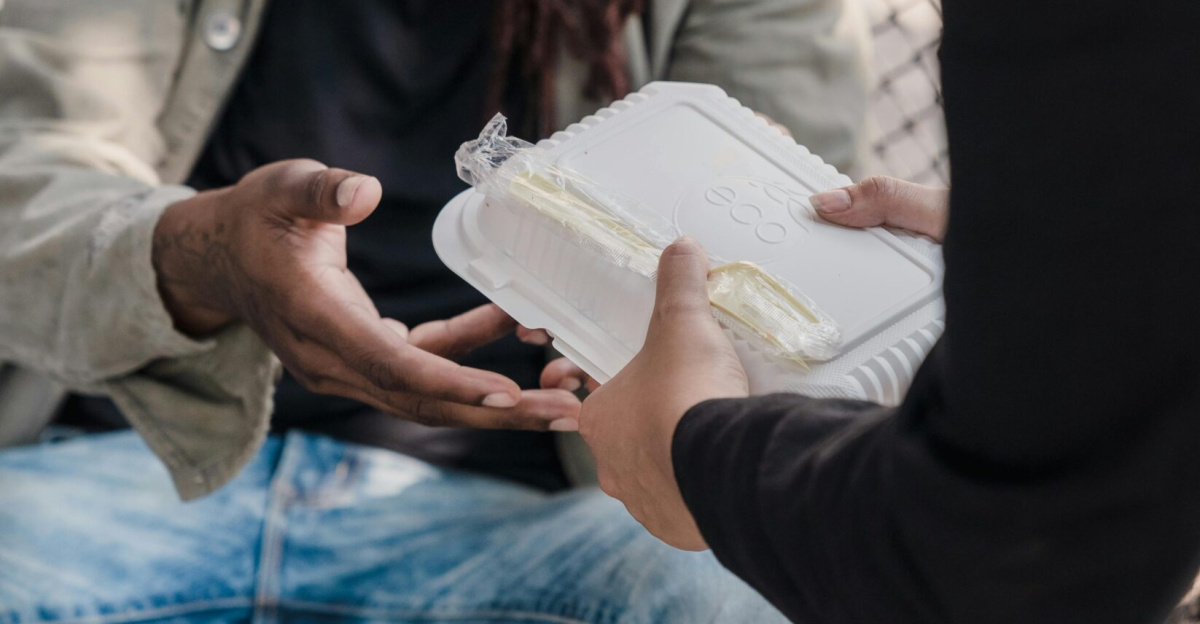 A person with dreadlocks receiving a meal from a helping hand on the street, showcasing kindness.