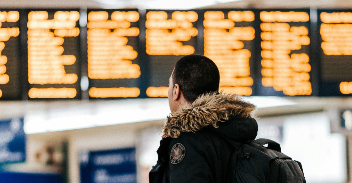 man standing inside airport looking at LED flight schedule bulletin board