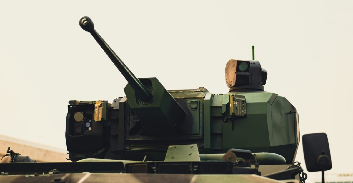 A military tank driving down a road next to a field