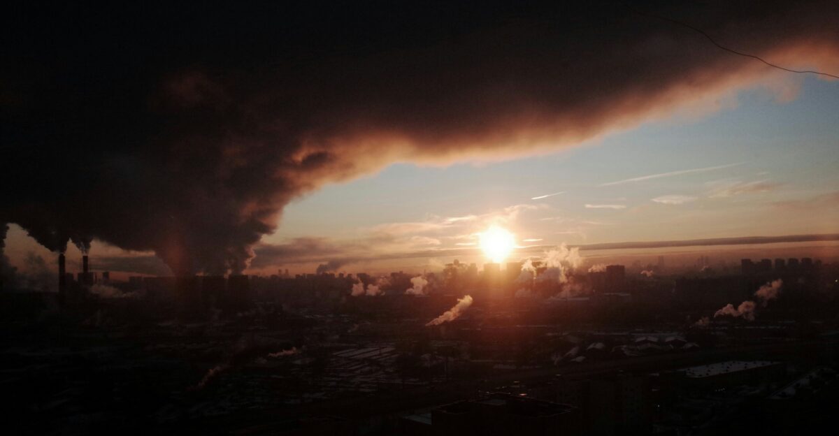 The sun is setting behind a smoke stack