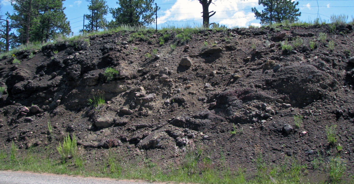 Lahar in the Tertiary of Colorado, USA.
<p>"Lahars" are simplistically defined as volcanic mudflows - volcanic ash mixed with water (derived from melted snow or rain).  In reality, lahars are not restricted to fine-grained sediments suspended in water.  Lahars are flood events that can include relatively little gravel or an abundance of gravel - sometimes very coarse-grained.
</p><p>A lahar can be a debris flow, with about two-thirds sediments and one-third water.  Debris flows are so sediment-concentrated that boulders are suspended and stay at the top when the flow stops - debris flows have large rocks at the surface.  This type of lahar is like wet concrete in consistency - it has a high viscosity.  Once moving, such flows become sheared and end up moving quickly, more quickly than water.
</p><p>A lahar can be more dilute than debris flows.  Hyperconcentrated flows have abundant fine-grained sediments held in suspension by turbulence.  The sediment volume of hyperconcentrated flows varies - they can be clay-rich or sand-rich, with 10% solids and 90% water to a 50-50 mix.  Such flows can also have large clasts, but when actively flowing, any large rocks will appear occasionally at the surface, then disappear below.  Traditionally, a flow with less than 50% gravel is called a "mudflow".
</p><p>The Tertiary-aged lahar seen here is south of Florissant National Monument in Colorado, a famous locality for well-preserved fossils in an ancient lake deposit ("Lake Florissant").
</p>
<hr>
<p>Info. from the National Park Service's Florissant Fossil Beds National Monument website:
</p><p>At the roadcut you can see the lahar that originated from the Guffey volcanic center to the west. This lahar impounded the river and created Lake Florissant. The lake was about a mile wide and extended 12 miles northwards. The debris carried by the flow contained rock fragments of different size, shape, and composition. The dark fragments are pieces of Thirtynine Mile andesite (a dark, fine-grained volcanic rock that originated from the Thirtynine Mile Volcanic Complex), while the lighter, pinkish fragments are pieces of 1.4 billion year old Cripple Creek Granite that was exposed to the surface during the Laramide Orogeny. Rounded fragments may have been picked up from the paleovalley through which the lahar flowed.
</p>
<hr>
<p>Stratigraphy: lower member, Thirtynine Mile Volcanics (Thirtynine Mile Andesite), Upper Eocene, 34-36 Ma
</p>
Locality: Route 1 roadcut ~0.2 kilometers south of Evergreen Station, northwest of the town of Cripple Creek, central Colorado, USA (38° 49' 07.34" North latitude, 105° 15' 33.85" West longitude)