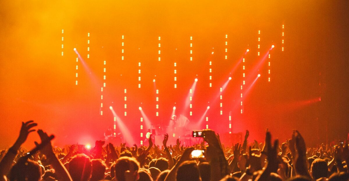 Energetic crowd at a live concert with bright stage lights and hands raised in celebration