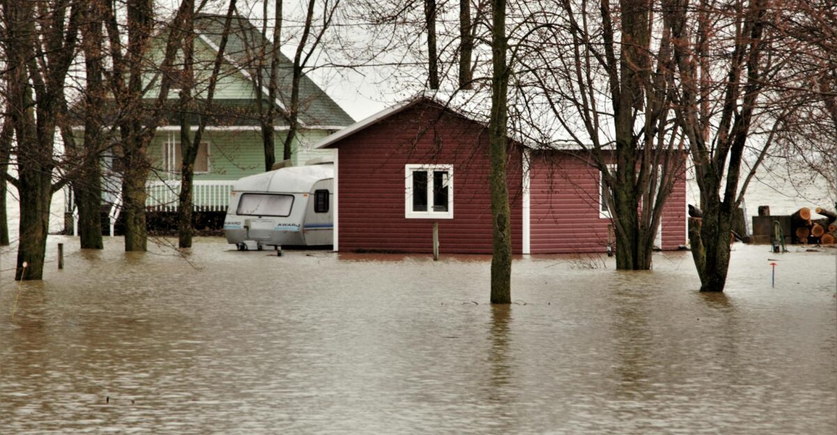 House and caravan surrounded by floodwaters among leafless trees in a natural setting
