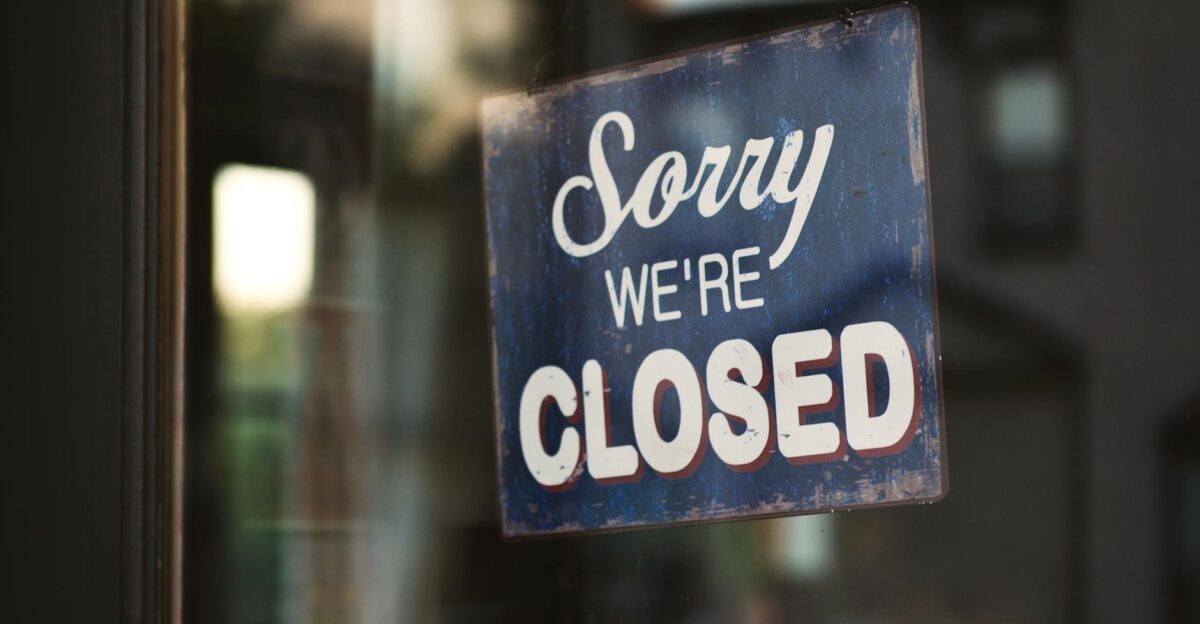 A vintage Sorry We re Closed sign on a glass door reflects street view outside