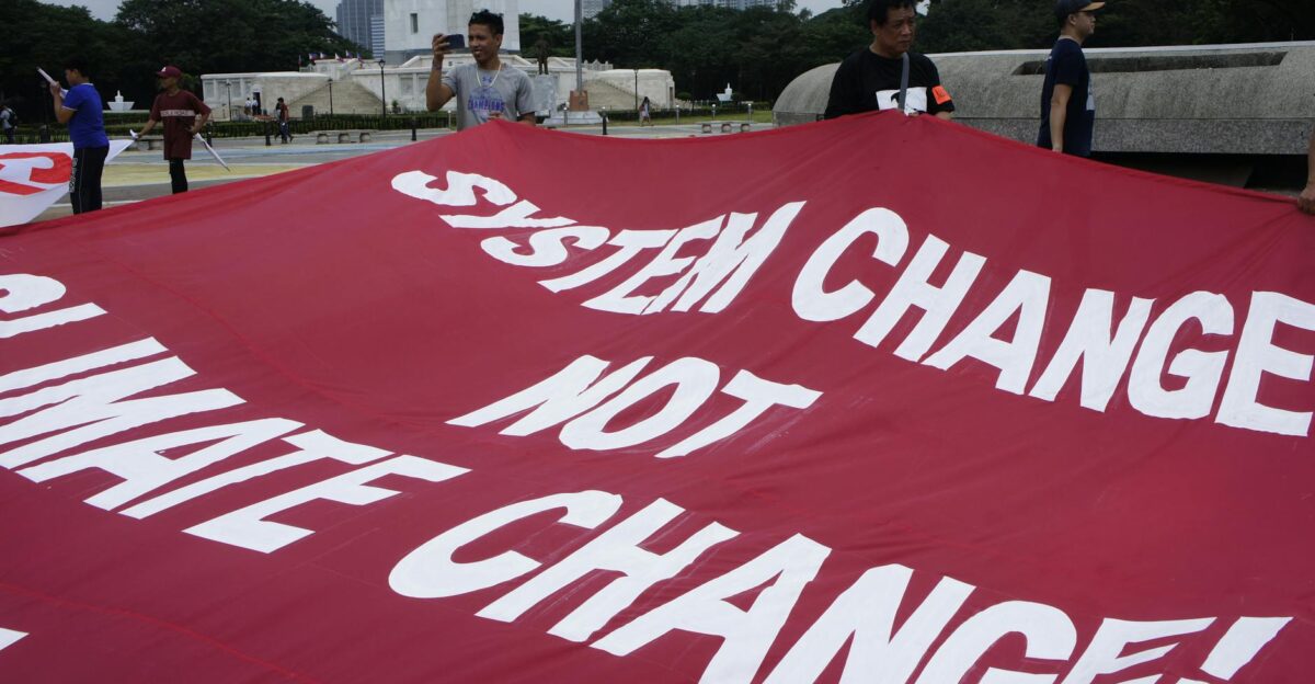 Protesters holding a red banner advocating System Change Not Climate Change in an outdoor setting