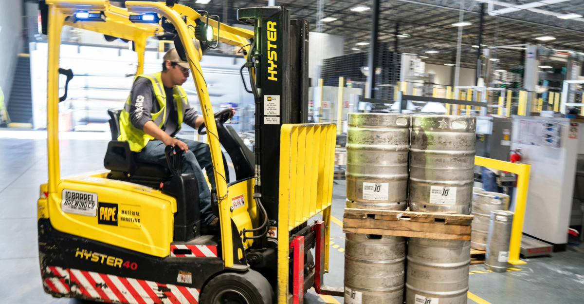 Forklift operator in warehouse moving beer kegs for distribution.
