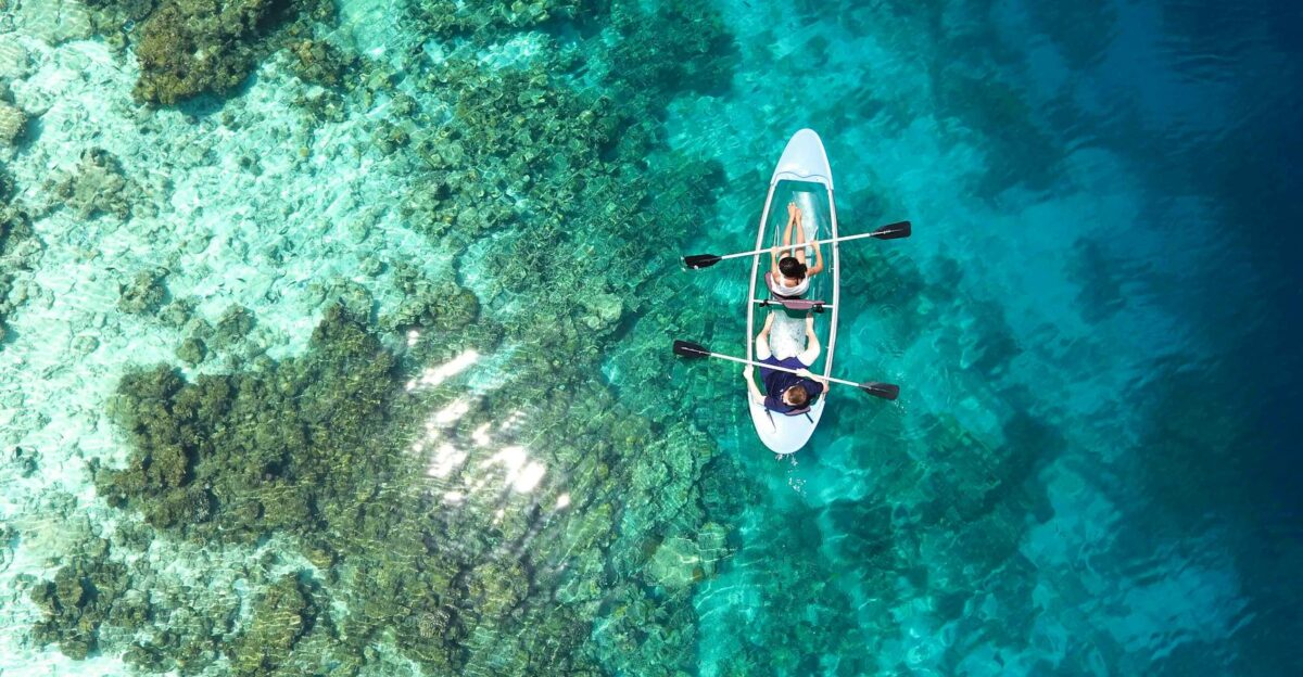 Aerial view of clear canoe gliding over vibrant coral reefs in the Maldives turquoise waters