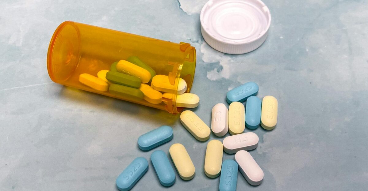 An open prescription bottle with assorted pills on a light blue background high angle view