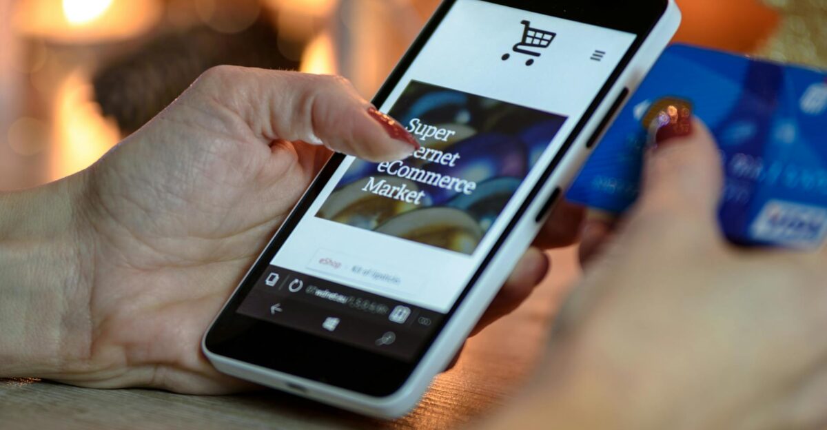 Woman using smartphone for online shopping with credit card in hand festive background lighting