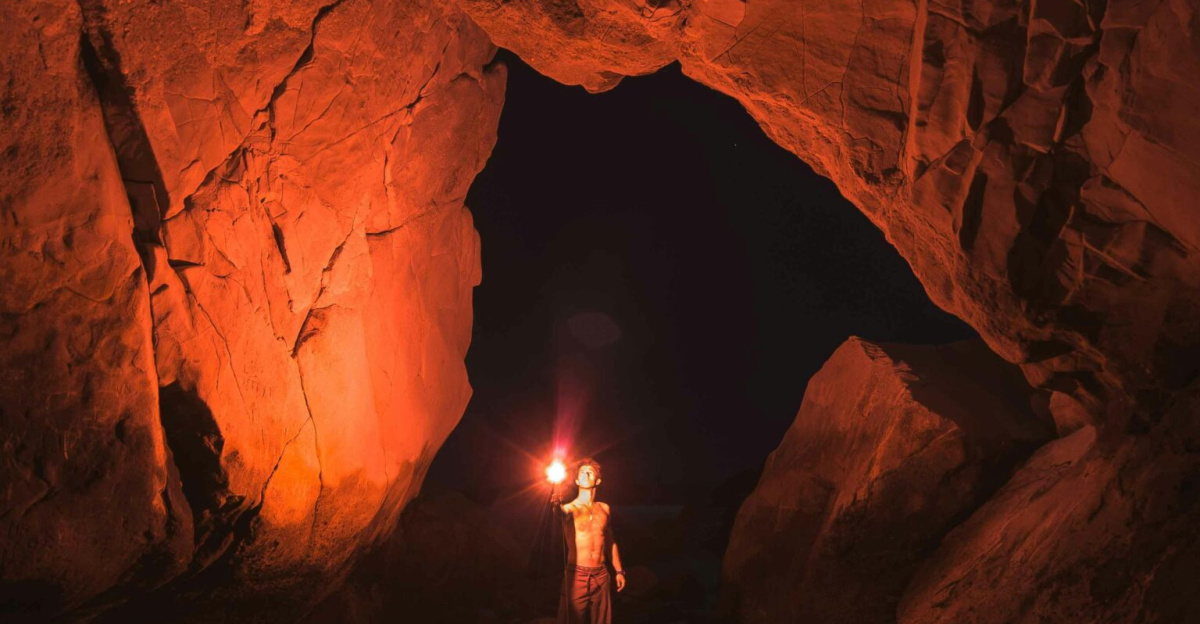 A lone adventurer illuminates a vast Californian cave with a torch at night.