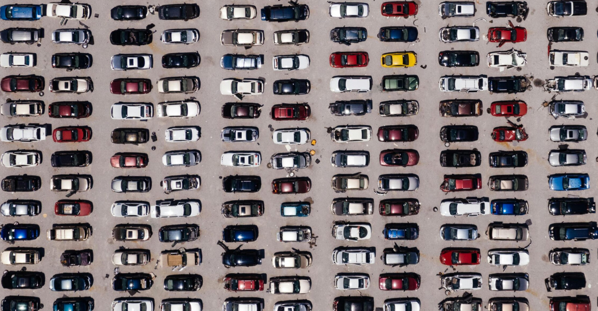 Top-down aerial shot of a large parking lot filled with rows of cars, showcasing organized symmetry.
