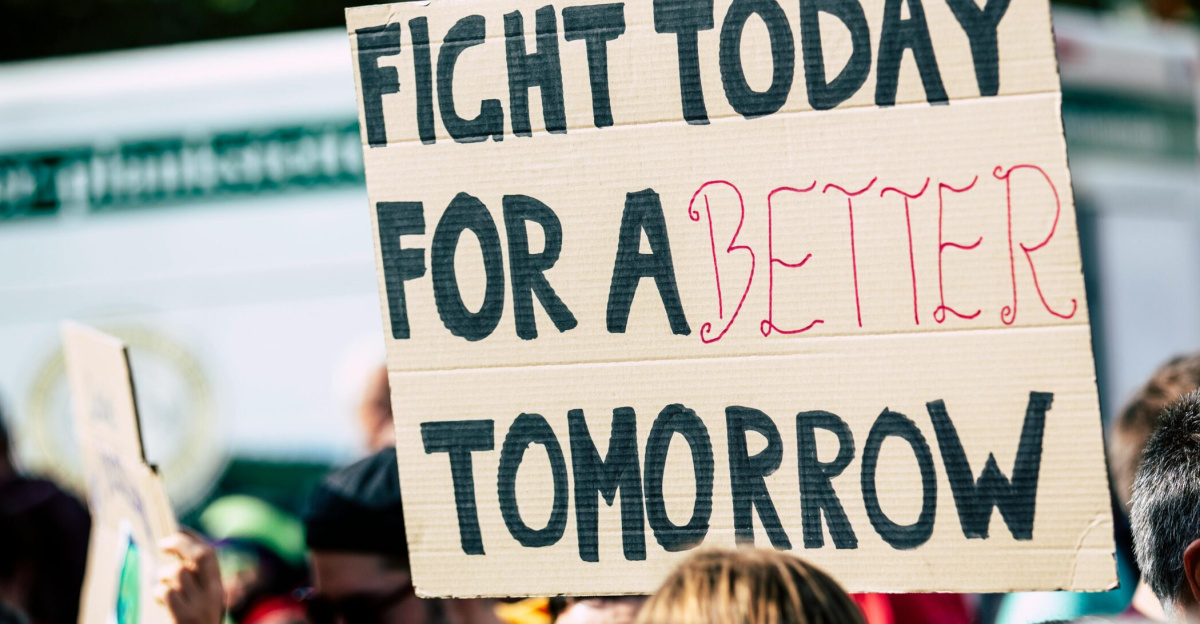 Crowd holding a protest sign with 'Fight Today for a Better Tomorrow', outdoors and during the day.