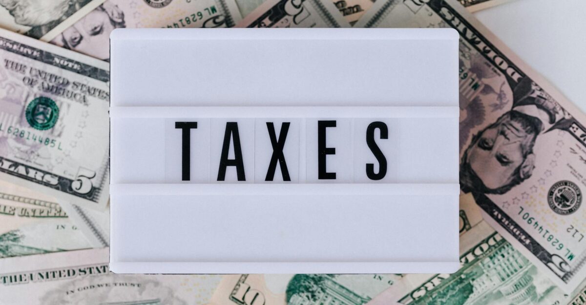 Top view of white vintage light box with TAXES inscription placed on stack of USA dollar bills on white surface