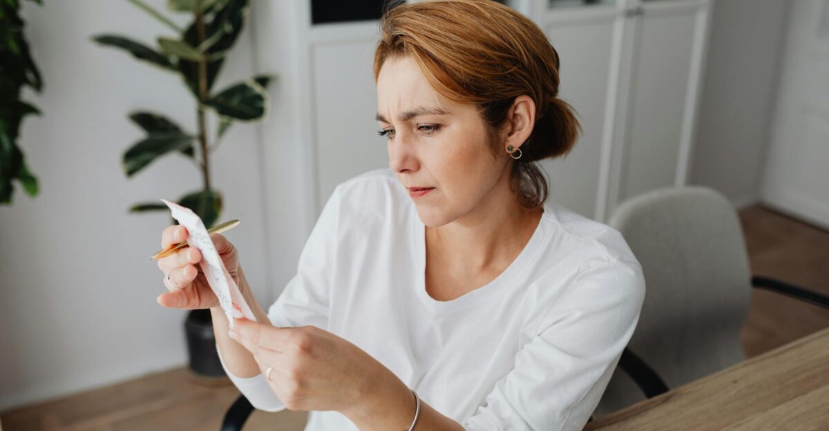 A concerned adult woman examines a receipt while sitting at her office desk indicating financial scrutiny