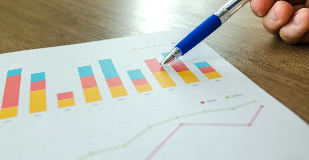 Detailed close-up of a hand pointing at colorful charts with a blue pen on wooden surface