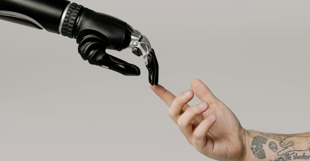 A human hand with tattoos reaching out to a robotic hand on a white background