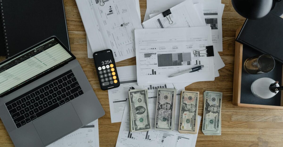 Overhead view of financial documents cash and technology on a wooden desk