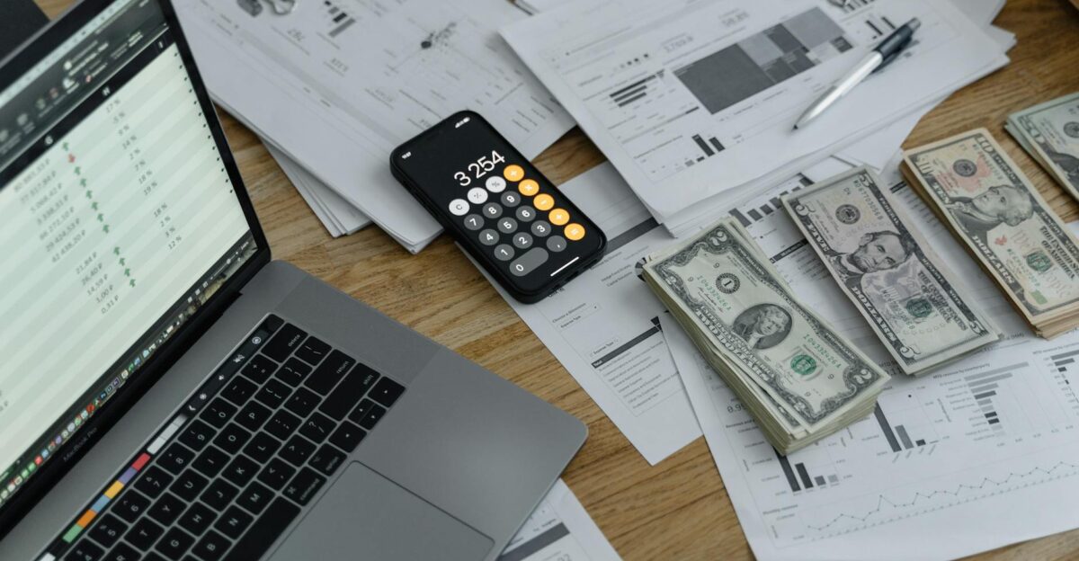 A desk with financial documents currency a laptop and phone calculator