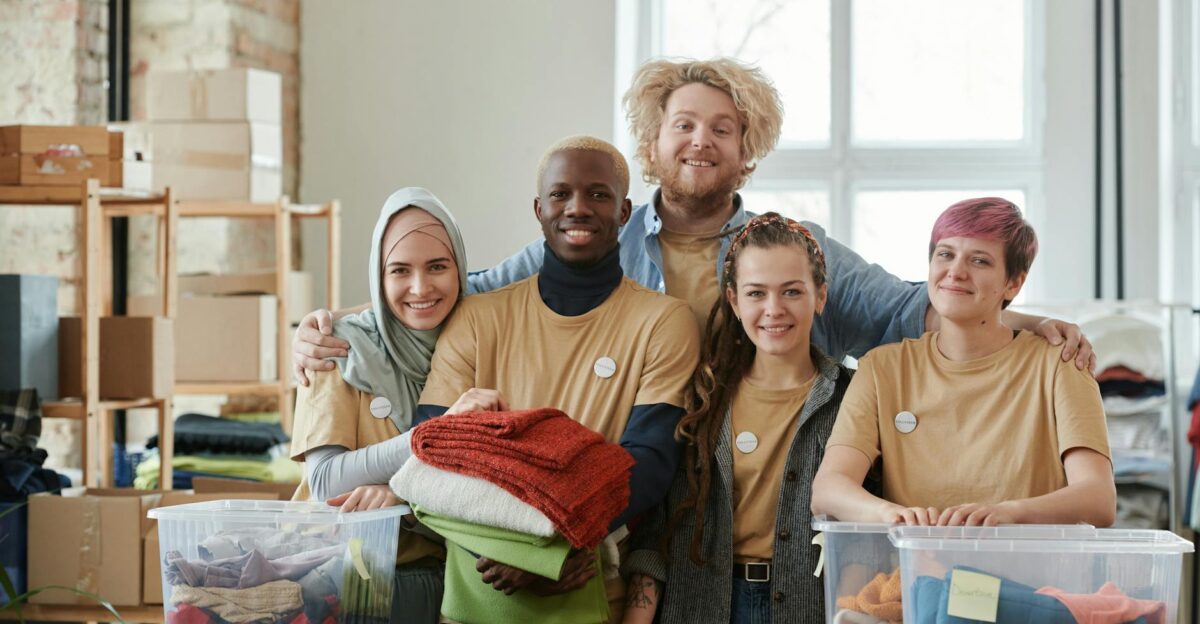Group of diverse volunteers smiling while sorting clothes at a charity donation center