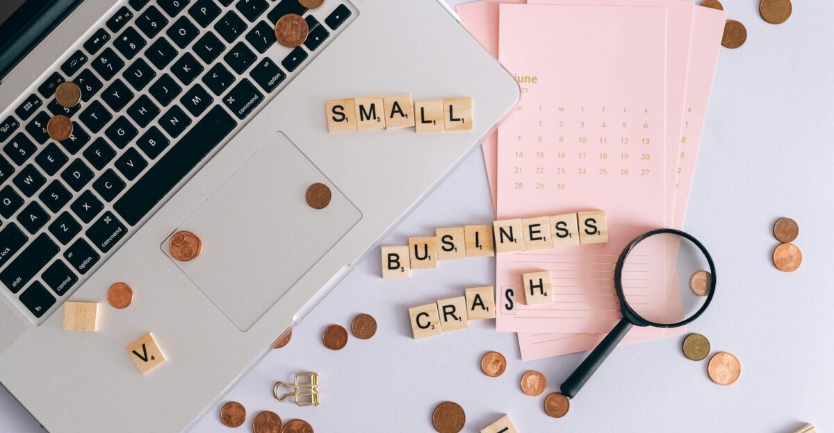 Flatlay of a laptop coins and scrabble tiles spelling small business crash