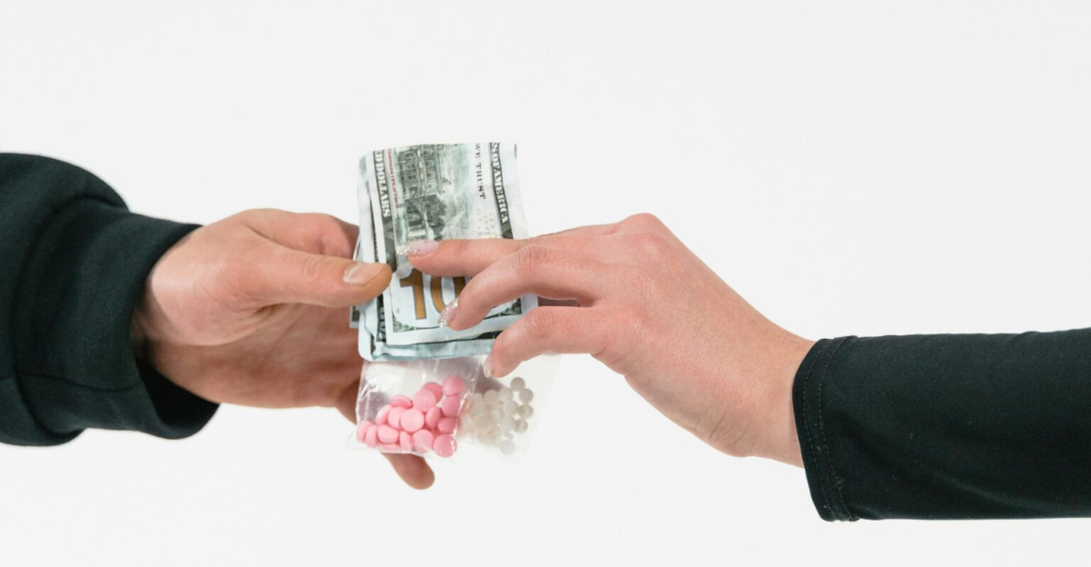 Two hands exchange pills and cash, symbolizing a transaction against a white backdrop.