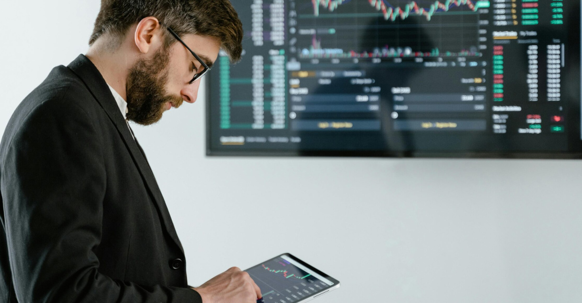 Professional man using tablet in front of cryptocurrency trading screen indoors.