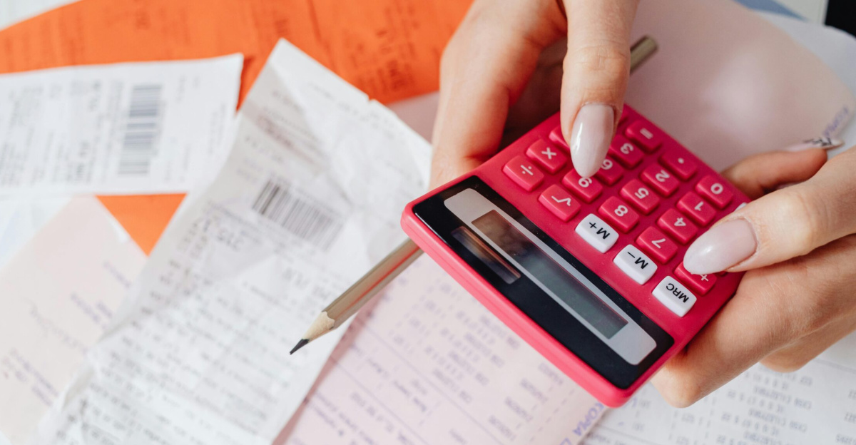 Hands using a pink calculator to manage expenses amidst various receipts and documents.