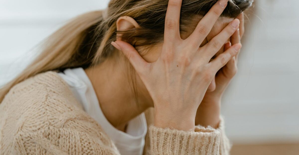 Woman sitting indoors with face covered by hands expressing stress and frustration