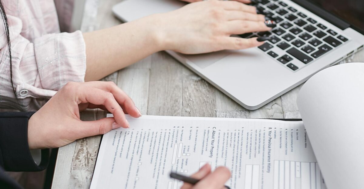 Close-up of hands typing on a laptop and reviewing business documents focused on finance and legal tasks