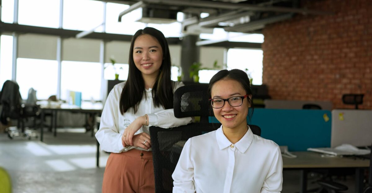 Two professional women smiling at camera in a modern office environment showcasing teamwork