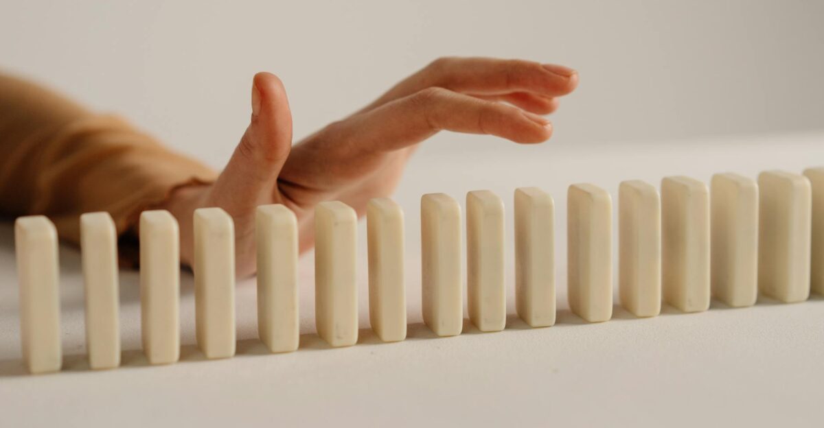 A hand poised to stop falling dominoes depicting control and intervention