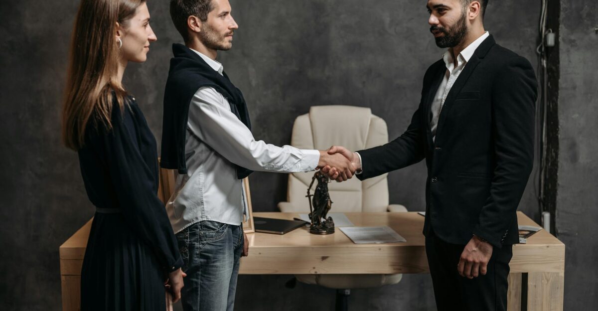Three business professionals engage in a formal handshake in a modern office setting