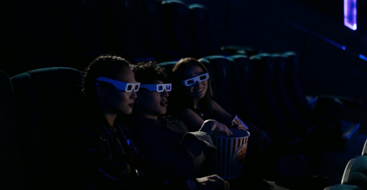 Group of friends wearing 3D glasses enjoying a film at a cinema with popcorn