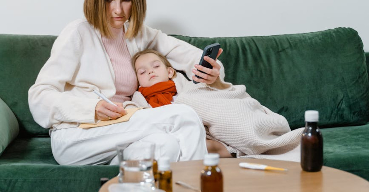 A mother comforts her sick child on a sofa while holding a smartphone showcasing family care