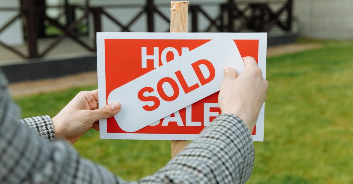 Close-up of hands placing a sold sticker on a real estate sign outside a house