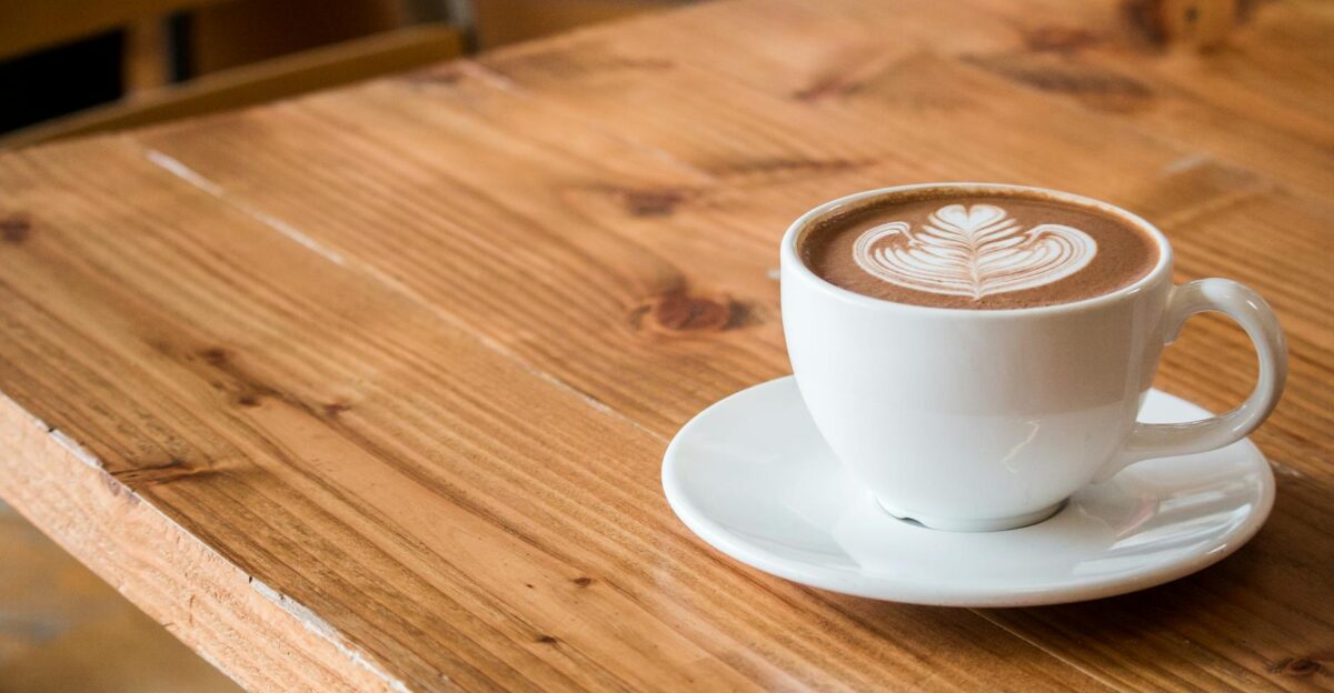 Close-up of a white cup of latte with artistic foam on a rustic wooden table