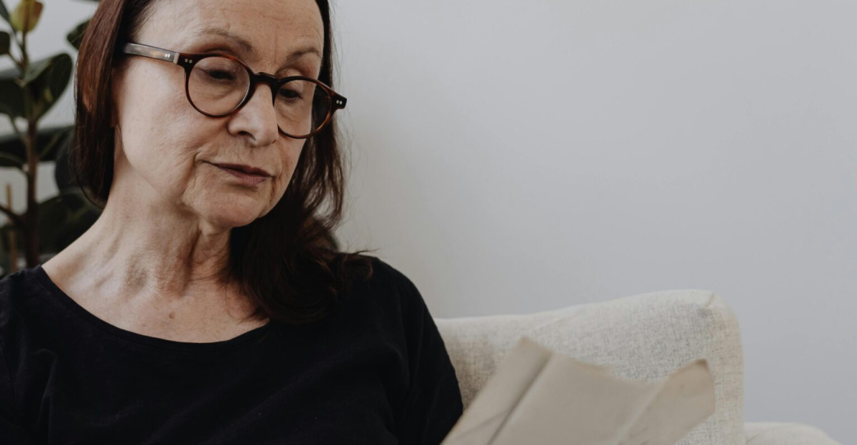 Senior woman sitting in an armchair indoors, reading letters, reflecting on memories and emotions.