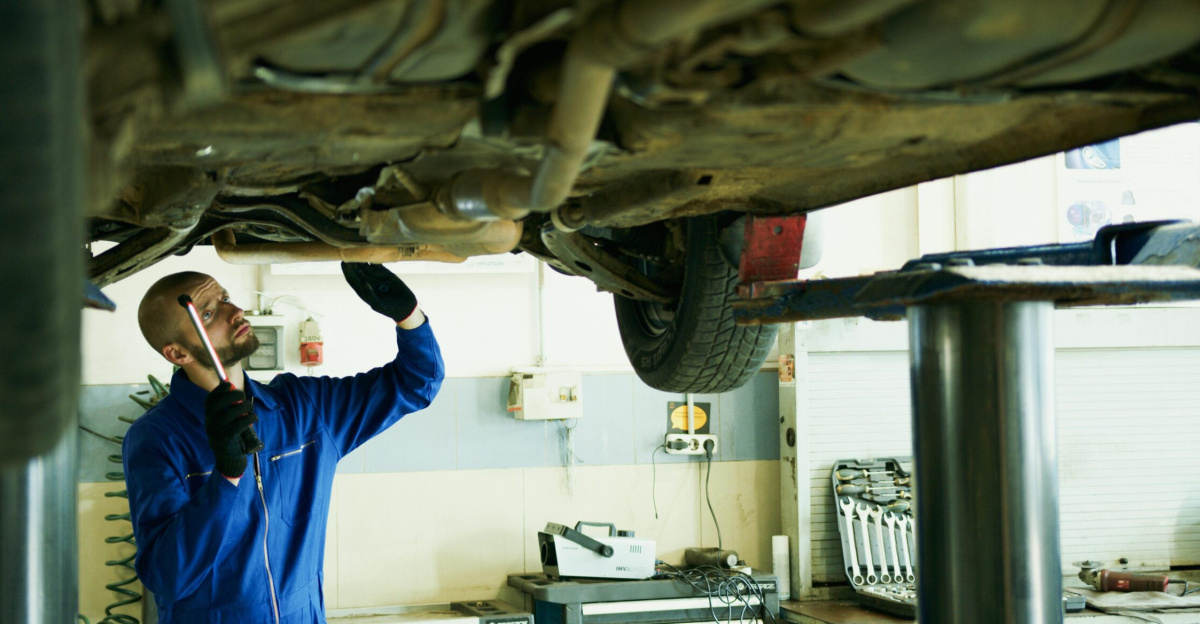 Mechanic inspecting a car's underside in a workshop for repairs.