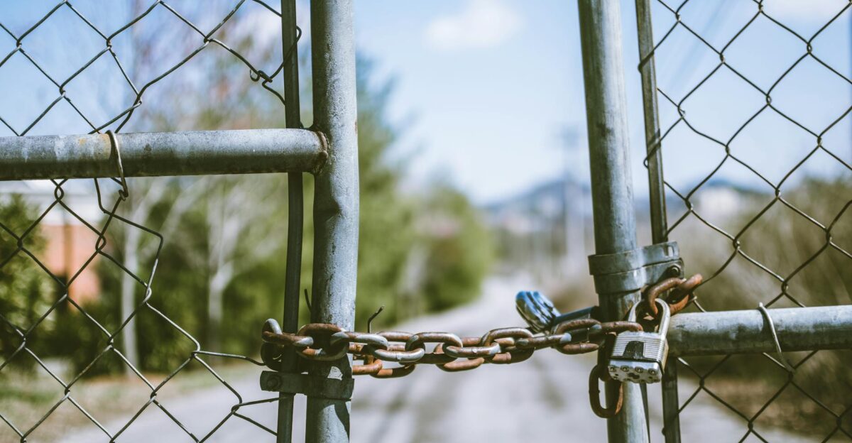 Close-up of a locked chain link fence with rusty chains and padlock outdoors in bright daylight