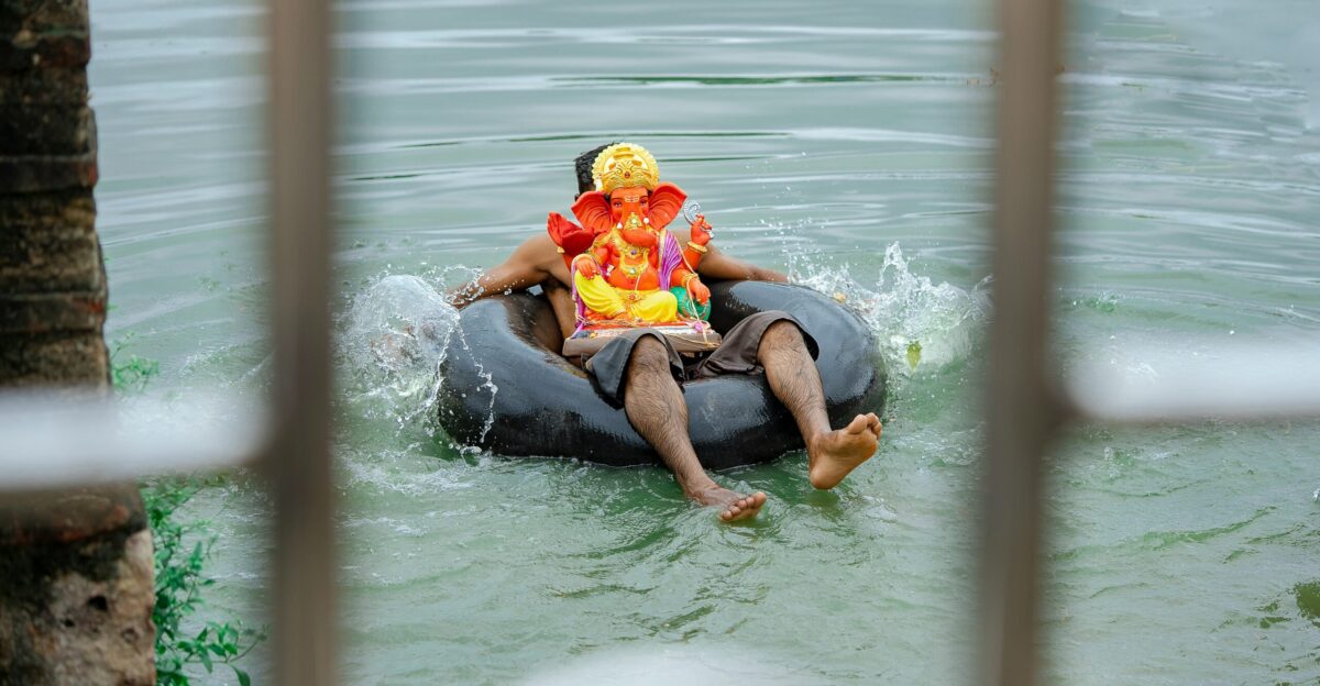 man with Lord Ganesha figurine on his belly sitting on black float on body of water during day
