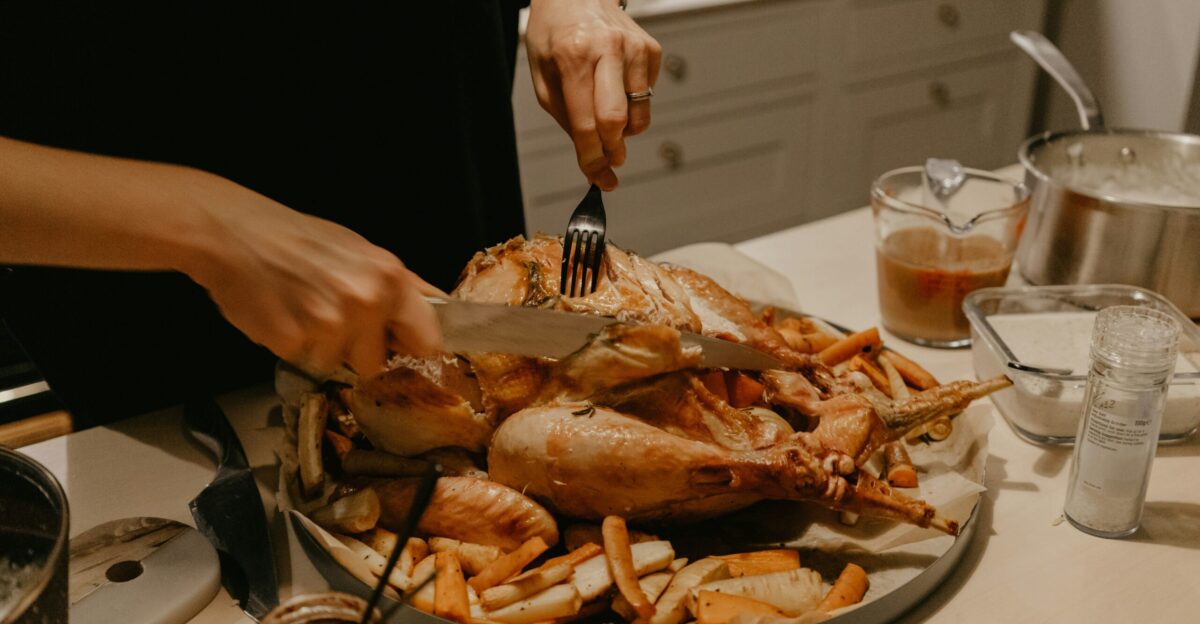 person holding stainless steel fork and bread knife slicing grilled meat on white ceramic plate
