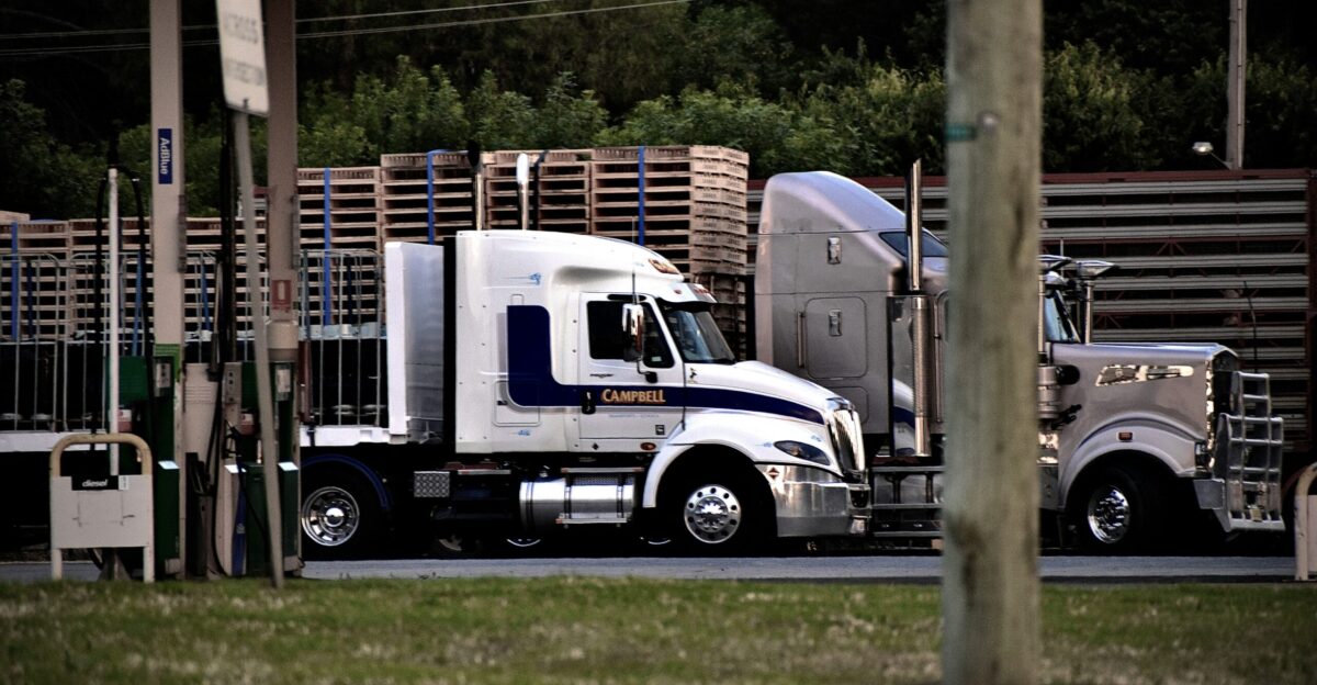 a semi truck driving down a street next to a wooden fence